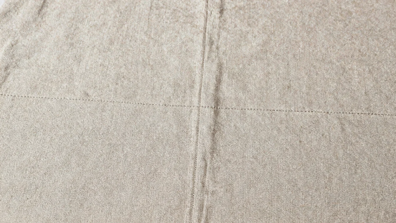 Editorial apparel photography, soft daylight, detail study of a woven fabric surface with visible weave and clean stitch