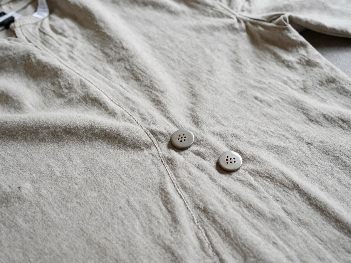 Editorial apparel photography, close detail of stitched clothing accessories laid on a neutral fabric surface, soft bala